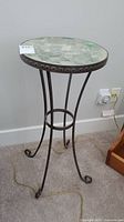 Full view of the metal plant stand showing the round mosaic top and curved metal legs.