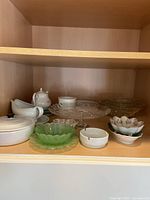 Shelved photo showing various serving dishes including ceramic covered pot, glass cake plate, decorative bowls and gravy boat.