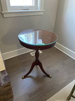 Front view of round side table showing glass top, wooden structure, and tripod legs with brass caps.