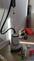 Full view of Conair fabric steamer with hose and nearby handheld vacuum and assorted items.