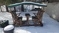 Front view showing two seats, central table, and canopy in snow.