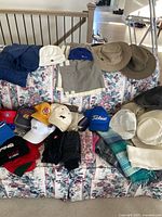 Photo of assorted men's hats, caps, gloves and a pair of pants displayed on floral sofa