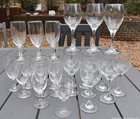 Photo showing the assortment of 25 clear wine glasses arranged on a table outdoors, displaying the variation in glass sizes.