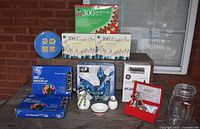 Full view of all Christmas light boxes, holiday decor including bowl, snowmen, bell, tin, and glass jar on outdoor table.