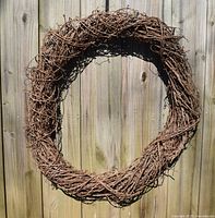 Full view of large handmade natural grapevine wreath hanging on wooden fence, showing irregular round shape and natural brown color.