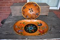 Front view of the round tole painted wooden bowl with floral cutout designs and oval wooden tray with hand painted floral patterns on a weathered surface.