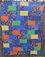 Full view of the colorful handmade quilt showing patchwork of solid colors and patterned fabric with animals, sports equipment, and trucks.