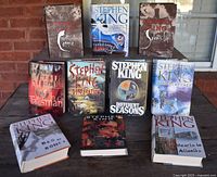 Photo showing all 10 hardcover Stephen King books with dust jackets arranged in two rows on a wooden surface.