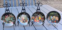 Four Bradford Exchange wall plates displayed on metal easels outdoors, showing detailed colorful Russian fairy tale illustrations.