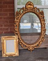 Two gold-tone ornate frames side by side with no glass, wooden box and a porch setting in background.