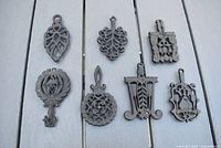 Top view of all seven cast iron mini trivets with various vintage intricate designs, arranged on a light gray surface.