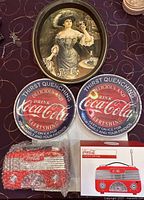 Two round Coca Cola melamine plates, Coca Cola CCR01 radio in bubble wrap, original radio box, and Pepsi Cola Gibson Girl tray with vintage artwork.