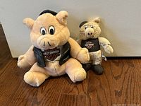 Photo of two Harley-Davidson Biker Hog Pig Plush Toys, one large and one small, both dressed in Harley biker clothing, sitting on a wooden floor.