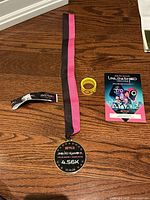 Photo showing the launch medal on a black and pink ribbon, yellow wristband, and Squid Game Unleashed game code card on wooden floor