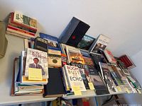 Wide view of a table with a large assortment of hardcover and paperback books arranged standing and lying flat. Titles visible include diverse subject matter from history to economics and nature.