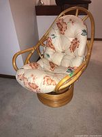 Full view of bamboo swivel chair with floral cushion in beige and red-orange tones.