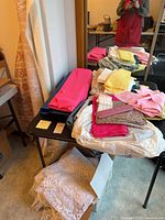 Fabric remnants and upholstery rolls on table including pink fabric, lace, yellow and beige pieces.