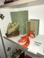 Shelf display of Buddha figurine on wooden base with Japanese Fuchin stones with tassels and boxes.