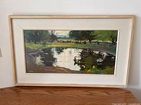 Full view of framed painting showing landscape scene and off‐white frame