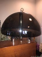 Full view of the vintage dome plastic hanging light fixture showing the smokey translucent dome and chrome base on a wooden surface.
