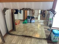 Full view of large rectangular mirror with wood frame and metal decorative corner/center accents, resting on floor against wall