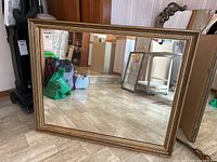 Full view of the rectangular mirror with wooden gold-toned frame placed on the floor against a wall.