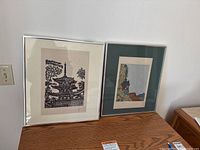 Two framed Asian themed prints side by side on a wood surface, showing the full frames and mats.