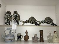 Shelf with decorative seahorses, marlin fish decorations, ceramic and textured ducks, ceramic teapot, ceramic stein beer mug, wooden pepper grinder, clear glass oil bottle and ceramic angel figurine.