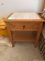 Front-facing view of the wood side table showing stone top, drawer with handle, and lower shelf.