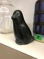 Soapstone bird carving on a white surface with glass jar and ceramic vase in background