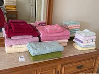 Photo showing multiple folded towels on a wooden dresser, including burgundy, pink, cream, blue, green, purple, white, and yellow colors.