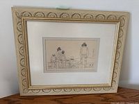 Front view of framed artwork showing decorative carved wood frame, white mat, and the ink drawing