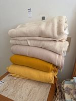 Stack of four folded blankets showing varying textures and colors, cream and yellow shades visible.