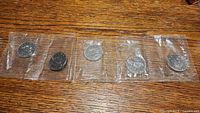 Five sealed Canadian dollar coins from 1969 laid out on a wooden surface, each individually wrapped in clear plastic packaging.