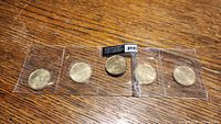 Five 2010 Canadian one-dollar coins still in original plastic holders, arranged on wooden surface.