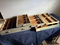 Five vintage wooden print block drawers laid out on a cloth surface, showing compartment divisions and metal handles.