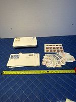 Overview of entire collection showing partial sheets of Canadian stamps, a stack of first day covers, and scattered loose stamps beside a measuring tape for scale.