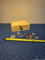 Photo showing the beige storage case with a fleur-de-lis pattern and the full set of Hard Rock Cafe pins laid out next to a measuring tape indicating case size approximately 10 x 7 x 4 inches.