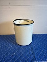 White enamelware pale with black rim and metal handle, front view showing some discoloration and wear.