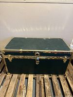 Front view of old steamer trunk on wooden pallet showing entire trunk and metal trim details.