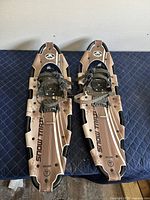 Pair of GV metal snowshoes side by side on a black quilted surface showing overall top view.