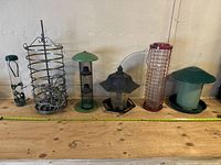 Front view of all six bird feeders in a row on wooden surface with measuring tape showing length and height