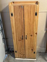 Front view of the two-door pine storage cabinet showing black metal hinges and handles, natural wood grain surface.