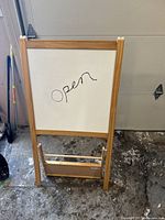 Photo of the sandwich board showing the white dry erase side with 'open' written on it, framed in wood.