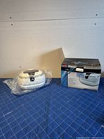 Photo of the ultrasonic jewelry cleaner unit wrapped in plastic, placed beside its original product box on a blue textured surface.