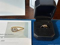 Ring displayed in black jewelry box alongside appraisal certificate showing overall appearance and box presentation