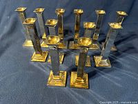 Front angled view of 12 matching brass candlesticks showing their two-tone finish with both silver and gold colors visible.
