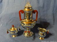 Full set of the antique coffee urn samovar with sugar container and creamer displayed against a blue-grey backdrop.