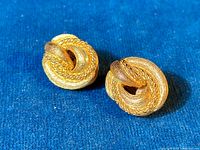 Pair of vintage 1980's Christian Dior gold tone clip-on earrings shown from front on blue background.