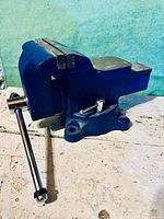 Full side angle view of the steel bench vise showing the clamping jaws, handle, and swivel base with mounting holes.